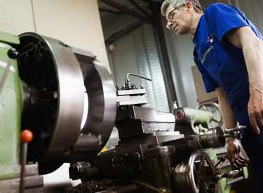 Worker in uniform operating in manual lathe in metal industry factory